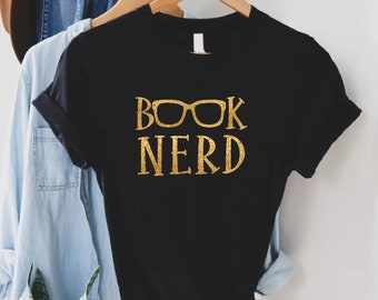 May include: Black t-shirt with gold glitter lettering that reads "BOOK NERD" with a pair of gold glitter glasses over the word "BOOK".