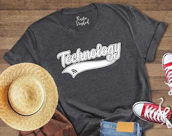 May include: A dark heather grey t-shirt with the word "Technology" in a white vintage-style font with a white baseball-style arc underneath. The shirt is laid out on a wooden surface with a straw hat, a brown leather backpack, blue jeans, and red sneakers.
