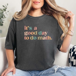 May include: Dark gray t-shirt with the text "it's a good day to do math" in colorful letters. The shirt is worn with blue jeans. The overall theme is education and learning.
