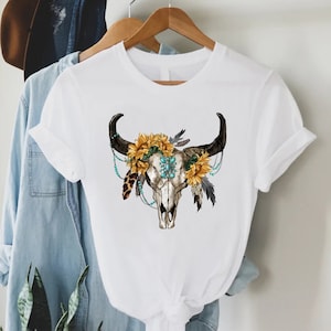 K&ouml;nnte beinhalten: Wei&szlig;es T-Shirt mit einem Aufdruck eines Kuhsch&auml;dels mit einer Sonnenblumenkrone und t&uuml;rkisfarbenen Perlen.