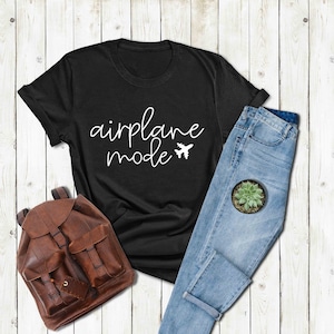 Puede incluir: Camiseta negra con texto blanco que dice "modo avi&oacute;n" y un peque&ntilde;o icono de avi&oacute;n.