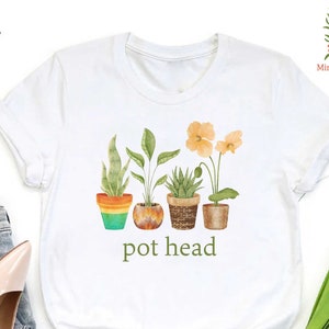 May include: White t-shirt with a green, orange, and brown illustration of potted plants and the text "pot head".