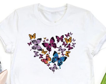 May include: White t-shirt featuring a heart-shaped design composed of colorful butterflies. The butterflies are in shades of pink, purple, orange, and blue. The shirt has short sleeves and a crew neck.