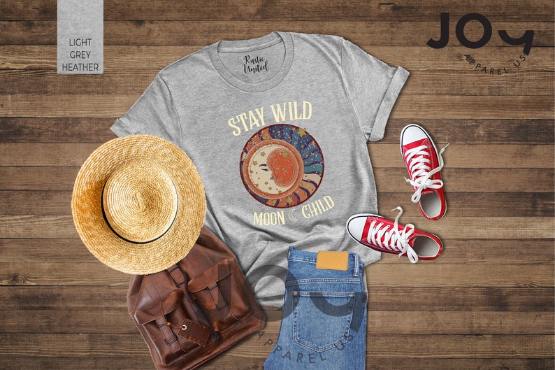 May include: A light grey heather t-shirt with the text "Stay Wild Moon Child" and a graphic of a crescent moon with stars and a sunburst design.