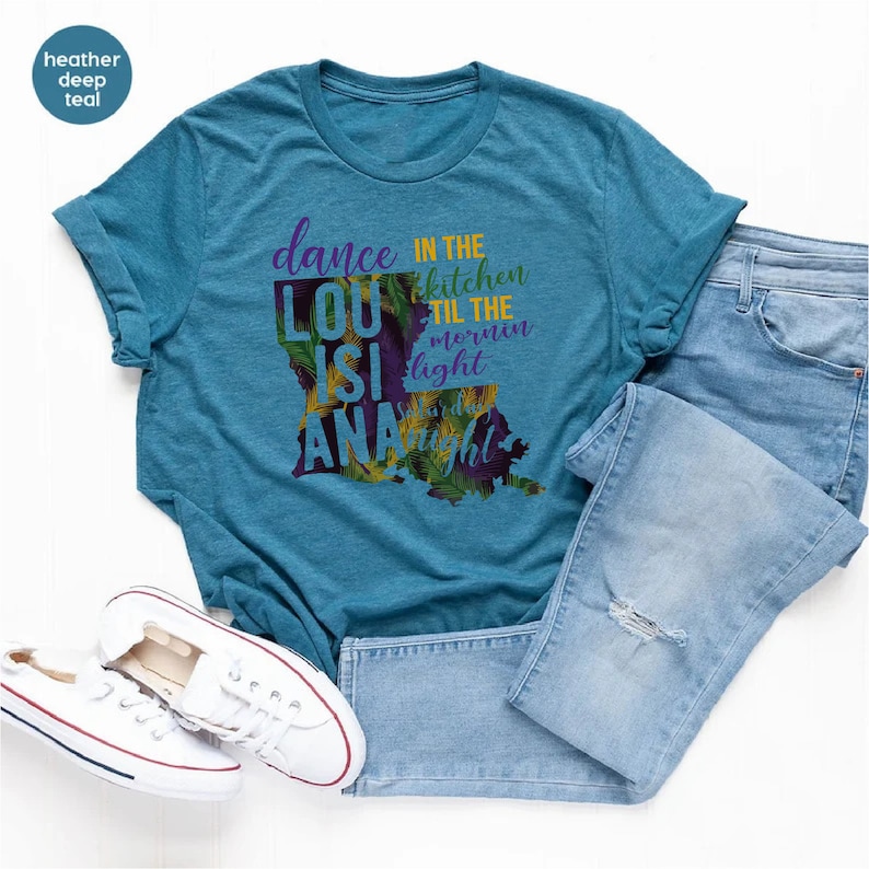 May include: A teal blue t-shirt with a graphic of the state of Louisiana. The graphic includes the text "dance in the kitchen til the mornin light" and "LouisiAna".
