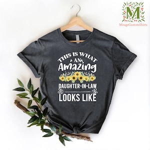 May include: Dark gray t-shirt with the text "This is what an amazing daughter-in-law looks like" in white. The text is surrounded by a floral design of yellow sunflowers.