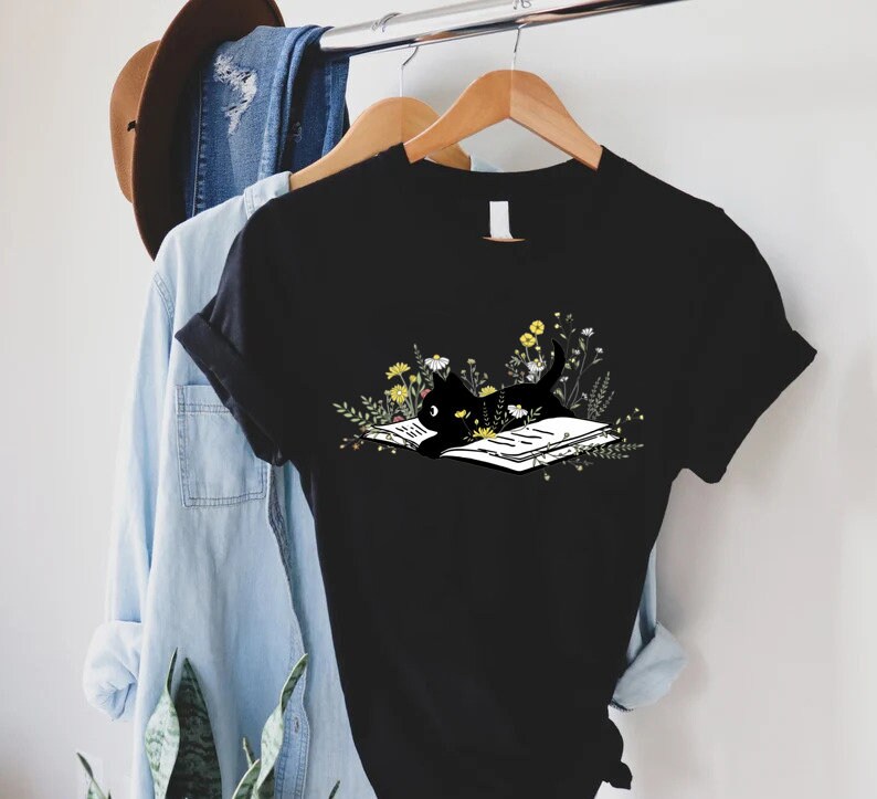 May include: Black t-shirt with a graphic of a black cat reading a book surrounded by flowers.