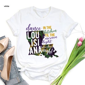May include: White t-shirt with a graphic of the state of Louisiana. The graphic includes the text "dance in the kitchen til the mornin light Saturday night" and the words "LouisiAna" are incorporated into the state outline.