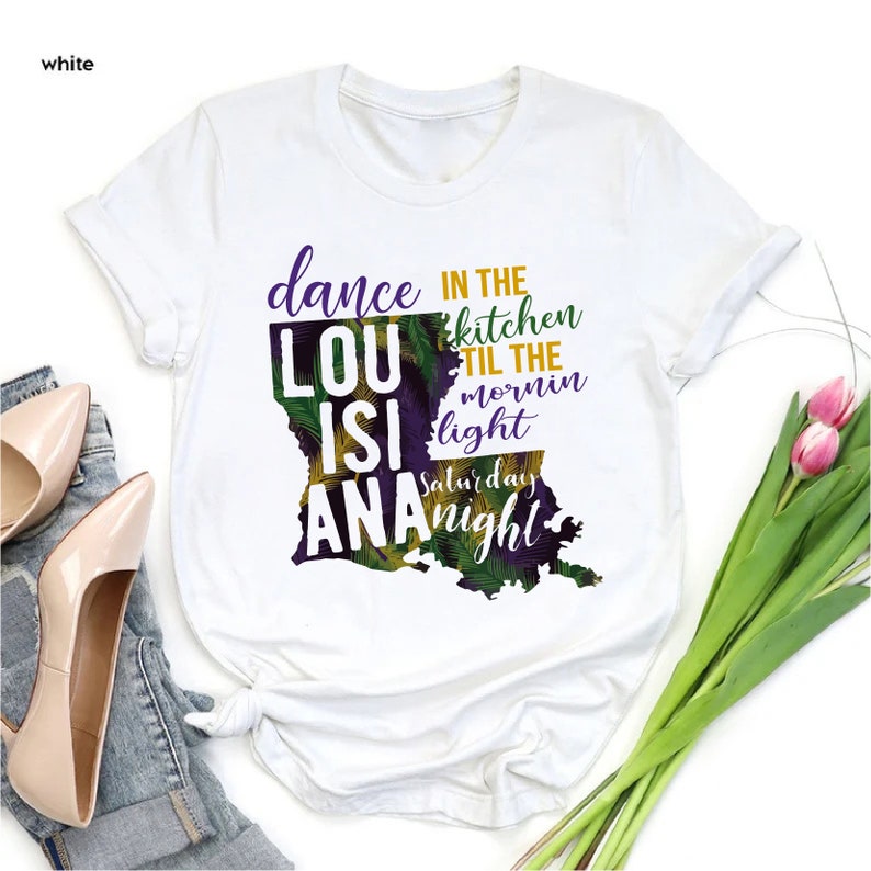 May include: White t-shirt with a graphic of the state of Louisiana. The graphic includes the text "dance in the kitchen til the mornin light Saturday night" and the words "LouisiAna" are incorporated into the state outline.