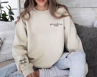 May include: A light beige sweatshirt with the text "grandma est. 2024" on the front and the text "Novella Briella" with a heart on the left sleeve.