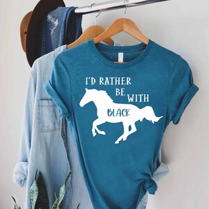May include: A teal blue t-shirt with a white silhouette of a horse and the text "I'd rather be with black".