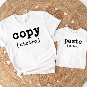 May include: Two white t-shirts with black text. The larger shirt says "copy (ctrl+c)" and the smaller shirt says "paste (ctrl+v)".