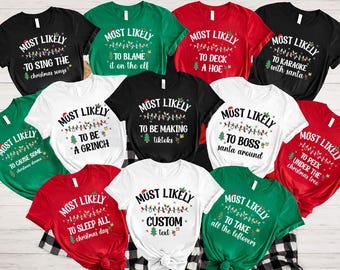 May include: Ten Christmas-themed t-shirts with different humorous sayings. The shirts are white, red, green, and black with a festive light string design. The sayings include "Most Likely to Sing the Christmas Songs", "Most Likely to Cause Some Christmas Drama", "Most Likely to Be a Grinch", "Most Likely to Blame it on the Elf", "Most Likely to Be Making TikToks", "Most Likely to Deck a Hoe", "Most Likely to Boss Santa Around", "Most Likely to Karaoke with Santa", "Most Likely to Peek Under the Christmas Tree", "Most Likely to Sleep All Christmas Day", "Most Likely to Take All the Leftovers", and "Most Likely Custom Text".