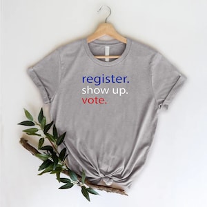 May include: A gray t-shirt with the text "register. show up. vote." in blue and red lettering.