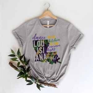 May include: Gray t-shirt with a purple and green outline of the state of Louisiana. The text "dance in the kitchen til the mornin light saturday night" is printed on the shirt.