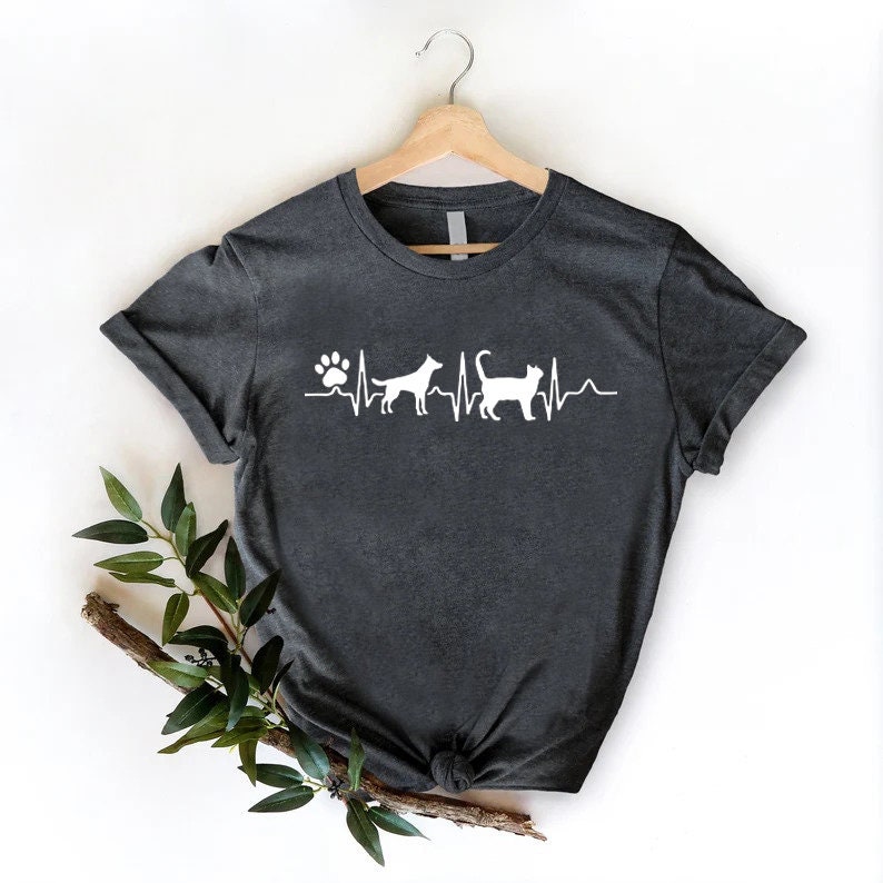 May include: A dark gray t-shirt with a white paw print and heartbeat graphic featuring a dog and cat silhouette. The shirt is on a hanger against a white background.