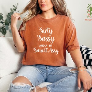 a woman sitting on a couch wearing a shirt that says sixty sassy and be