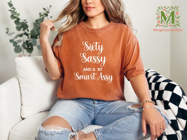 a woman sitting on a couch wearing a shirt that says sixty sassy and be