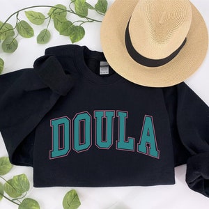 a black sweatshirt with the word doula on it next to a straw hat
