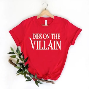 May include: Red t-shirt with white text that reads "Dibs on the Villain".
