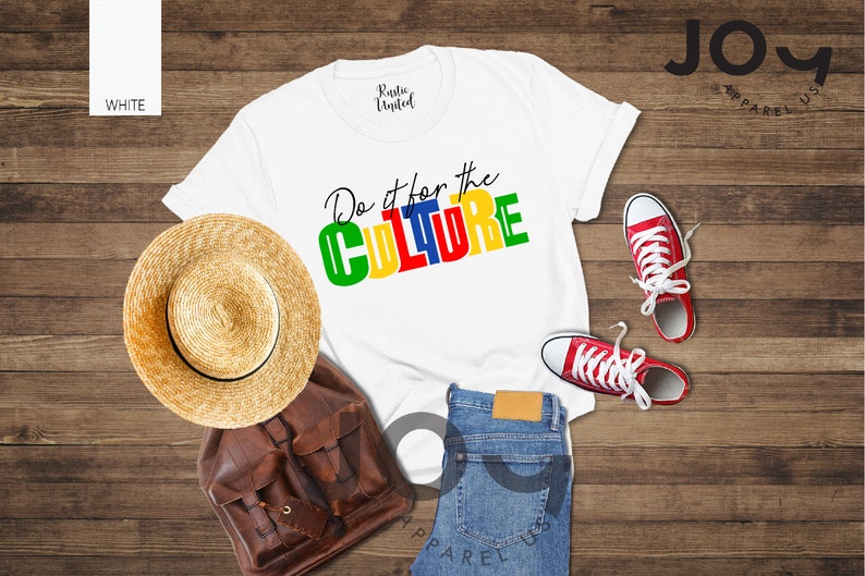 May include: White t-shirt with the text "Do it for the CULTURE" in colorful block letters. The shirt is laid out on a wooden surface with a straw hat, a brown leather bag, and red sneakers.