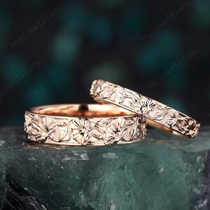 May include: Two rose gold wedding bands with a floral design. The bands are stacked on top of each other.