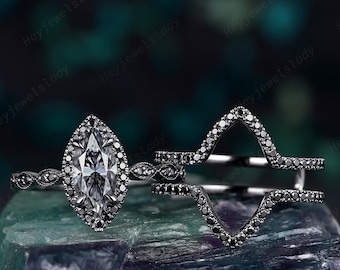 May include: A marquise-cut engagement ring with a halo of black stones, paired with a matching black diamond wedding band. The ring set is displayed on a textured, multi-colored surface. The brand name "Heyjewelslady" is visible.