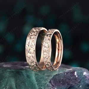 May include: A pair of rose gold wedding bands with a floral design. The bands are smooth and shiny.