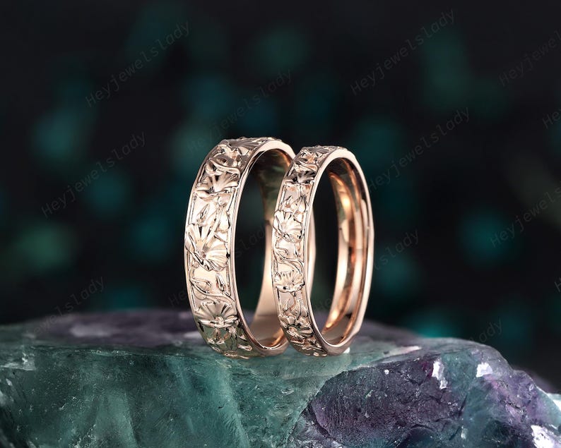 May include: A pair of rose gold wedding bands with a floral design. The bands are smooth and shiny.