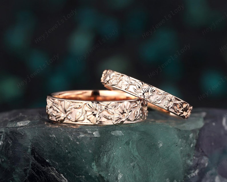 May include: Two rose gold wedding bands with a floral design. The bands are stacked on top of each other.