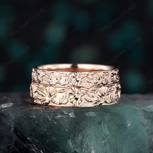 May include: A pair of rose gold wedding bands with a floral design. The bands are stacked on top of each other.