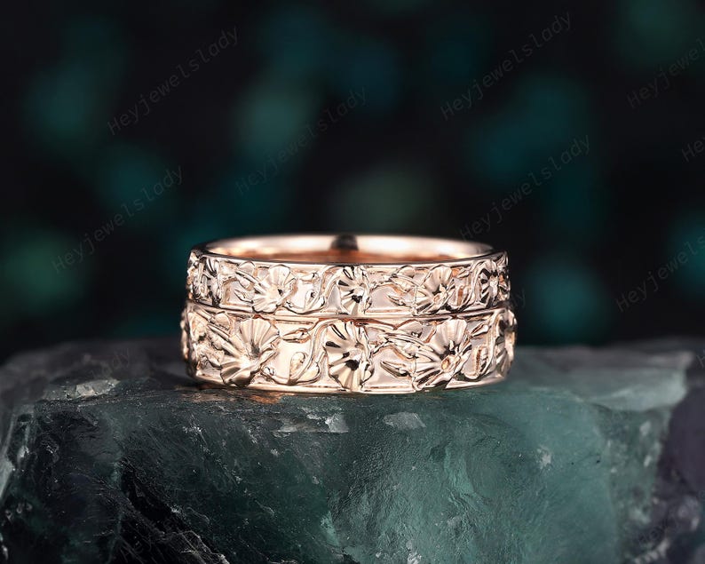 May include: A pair of rose gold wedding bands with a floral design. The bands are stacked on top of each other.