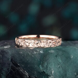 May include: A delicate rose gold band ring with a floral design. The ring is made of a thin band with a detailed floral pattern.