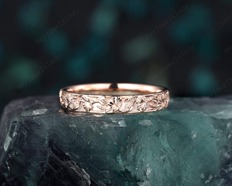 May include: A delicate rose gold band ring with a floral design. The ring is made of a thin band with a detailed floral pattern.