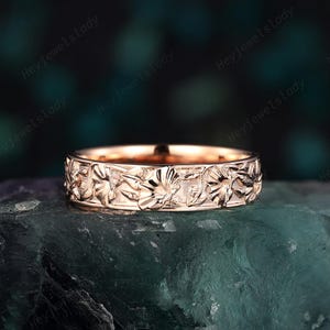 May include: A rose gold band ring with a floral design. The ring is made of metal and has a polished finish.