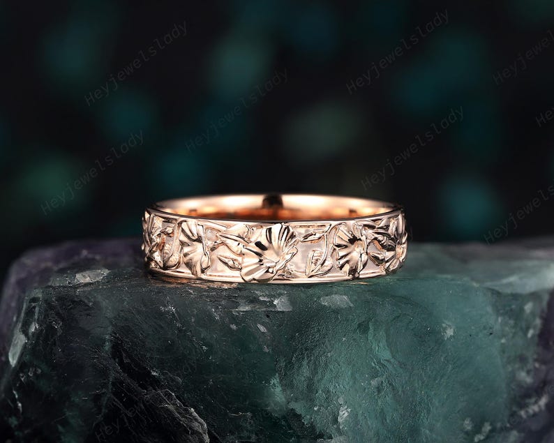 May include: A rose gold band ring with a floral design. The ring is made of metal and has a polished finish.
