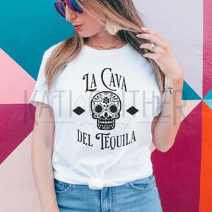 May include: White t-shirt with a black and white sugar skull graphic and the text "La Cava del Tequila".