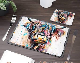 May include: A colorful, abstract painting of a Highland cow on a slate placemat and coaster set. The cow's fur is painted in shades of blue, pink, orange, and yellow. The background is white with splashes of color.