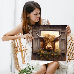 Op de afbeelding: Een schilderij van een Highland-koe met lange, harige bruine vacht die uit een raam in een houten schuur kijkt. De koe heeft een witte neus en grote, donkere ogen. Het raam staat open en er groeien bloemen omheen.