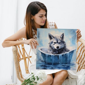 May include: A woman is holding a painting of a wolf sitting in a blue bathtub. The wolf is grey and white with blue eyes. The bathtub is filled with blue water and has a white rim. The background of the painting is a light blue sky with white clouds.