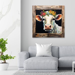 May include: A white cow with a colorful flower crown looks out from a rustic wooden frame. The cow's eyes are closed and its mouth is slightly open, as if it is smiling. The background is a dark blue color.