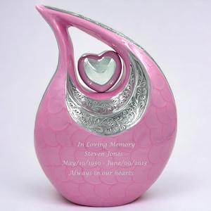 Op de afbeelding: Een traanvormige roze urn met een zilveren hartaccent en bloemmotieven. De urn is gegraveerd met de tekst: In Loving Memory, Steven Jones, May/19/1950 - June/09/2013, Always in our hearts.
