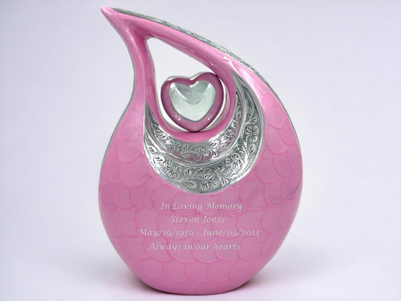 Op de afbeelding: Een traanvormige roze urn met een zilveren hartaccent en bloemmotieven. De urn is gegraveerd met de tekst: In Loving Memory, Steven Jones, May/19/1950 - June/09/2013, Always in our hearts.