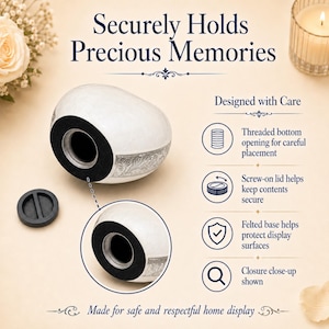 Op de afbeelding: Een witte, hartvormige urn met een zilverkleurige bloemenband. De urn heeft een opening met schroefdraad aan de onderkant, een schroefdeksel en een vilten basis. Tekst: Securely Holds Precious Memories, Designed with Care, Made for safe and respectful home display.