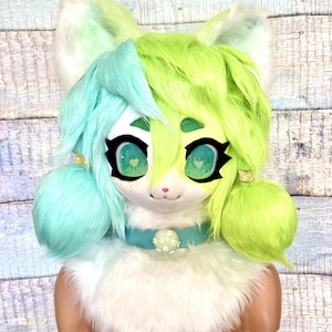 May include: A white furry cat head with green and blue hair, green eyes, and a blue collar with a white flower design.