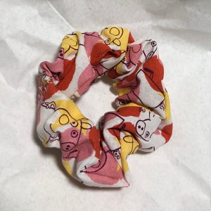 May include: A white, yellow, pink, and orange scrunchie with a cartoon pig pattern.