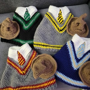 May include: Crocheted pet sweaters and hats in various colors, resembling school uniforms. The sweaters feature white collars and ties, with accents in green, yellow, red, and blue. The hats are brown and cone-shaped.