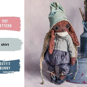 May include: A brown bunny wearing a blue and green outfit with a hat that says "I'm happy". The bunny is standing on a gray surface next to a metal container with paintbrushes.