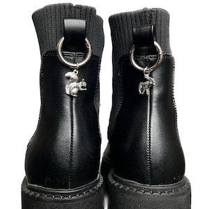 May include: A pair of black ankle boots with a knitted cuff and a silver charm hanging from each boot. The charms are a squirrel and a moose.