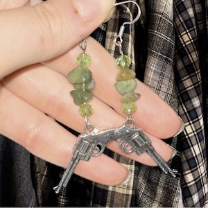 Puede incluir: Un par de pendientes de plata con dijes de pistola y cuentas de piedra verde y amarilla.
